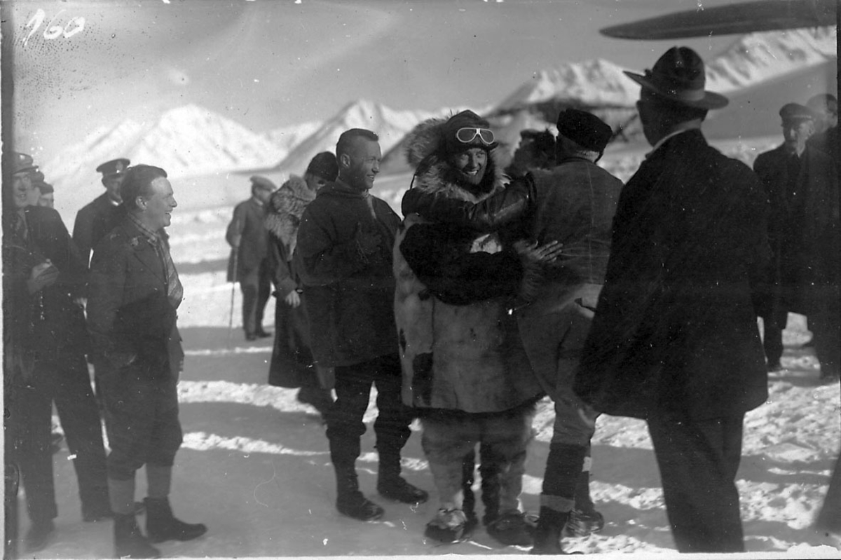 En gruppe personer, tatt utendørs. Litt av fly t.h., Fokker FVII "Josephine Ford". Snø på bakken.