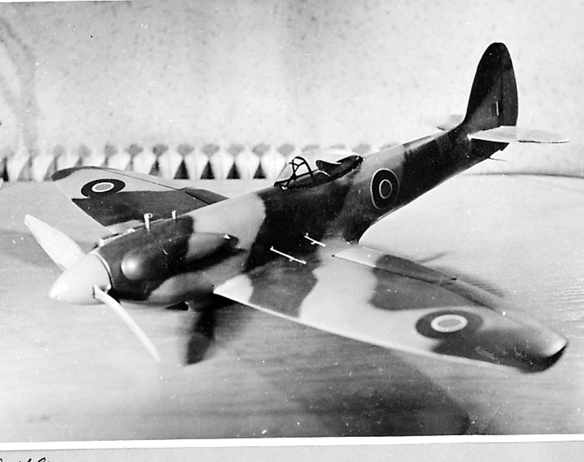 Fra album. 1 foto av modellfly, spitfire IV/XII oppstilt på en benk.