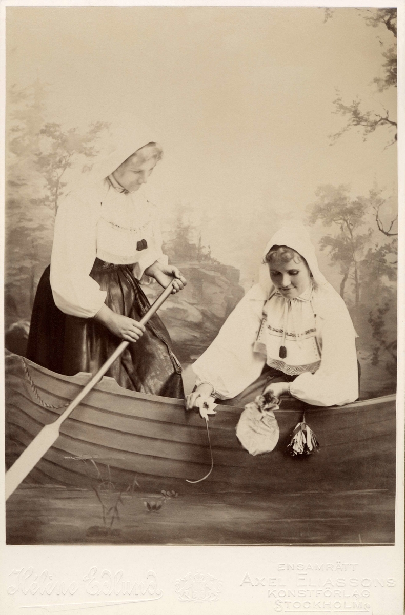 Två unga flickor poserar klädda i dräkt från Orsa, Dalarna med vita blusar och vita hättor.