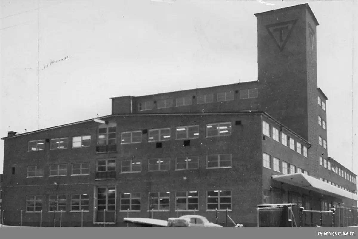 Gummifabriken. Byggnad 96, uppförd 1952-1953. Här tillverkades bland annat de första plastprodukterna efter kriget. Bilden tagen söderifrån. Utanför gummifabriken står en Wolksvagen.