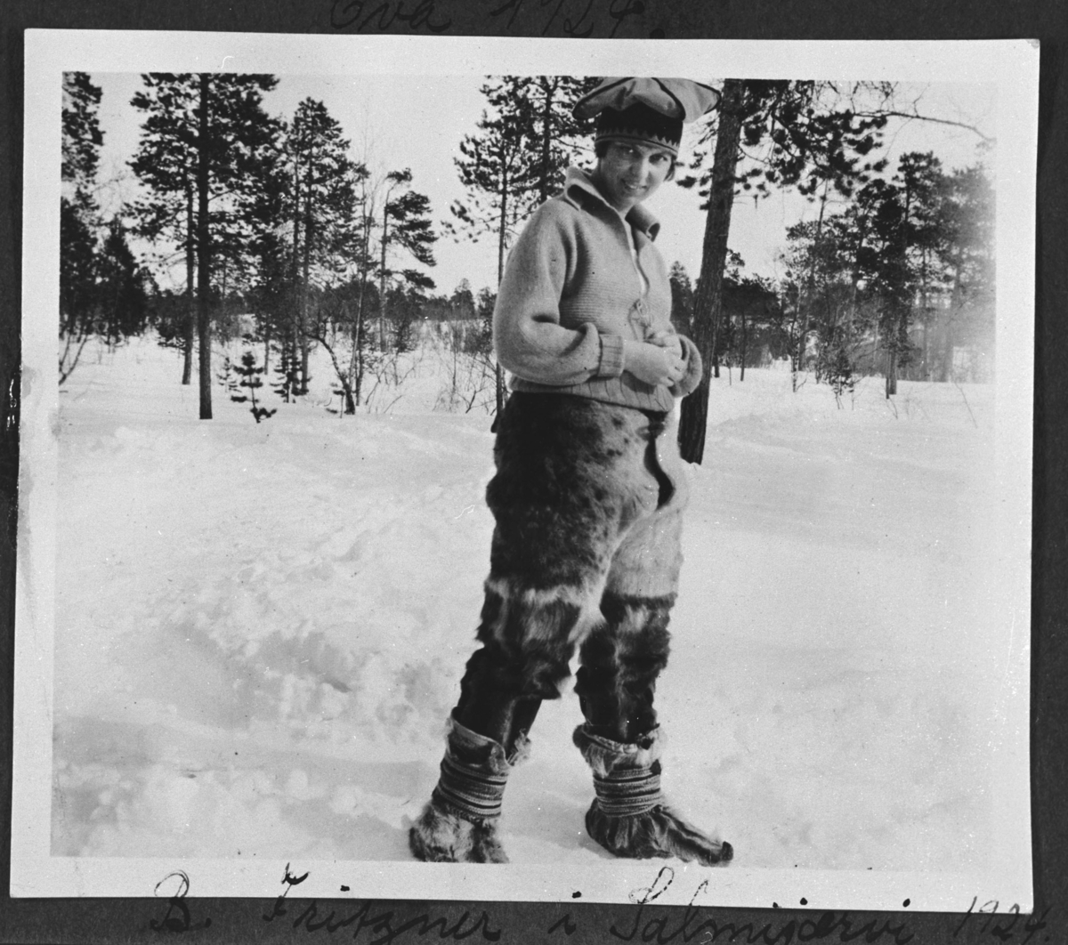 Ung samejente fotografert på vinter i Salmijärvi. Hun har på seg reinskinnbukse, genser og samehua.