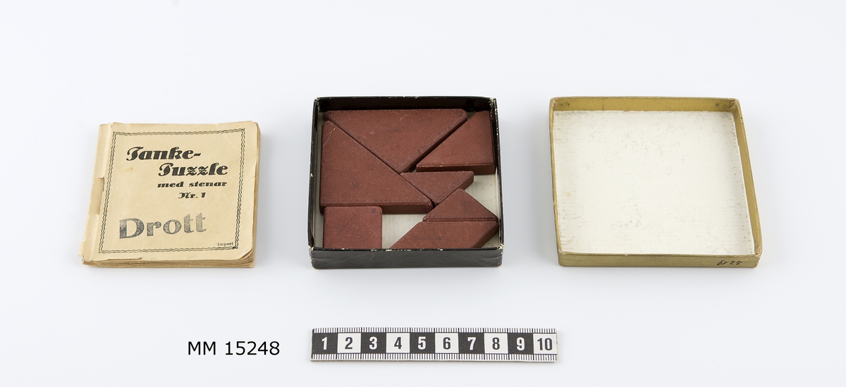 Tankepuzzle i en ask innehållande häfte och 7 stenar.
Ask, kvadratisk papp-ask med svart låda och guldfärgat lock.
Kvadratiskt häfte samt rödbruna olikformade stenar