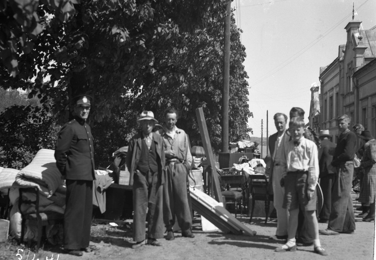 En politimann, flere menn og gutt ved gjenstandene til auksjonen i Biørnsborgparken, 5.06.1941.