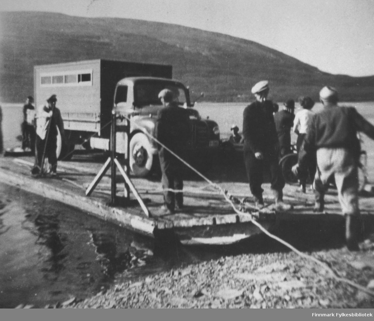 På ferge over Tanaelva ved Langnes, 1954. Hjemtur fra Kongsfjordfjellet. På bildet ser man ferga med en lastebil (Austin Loadstar) og noen mennesker ombord.