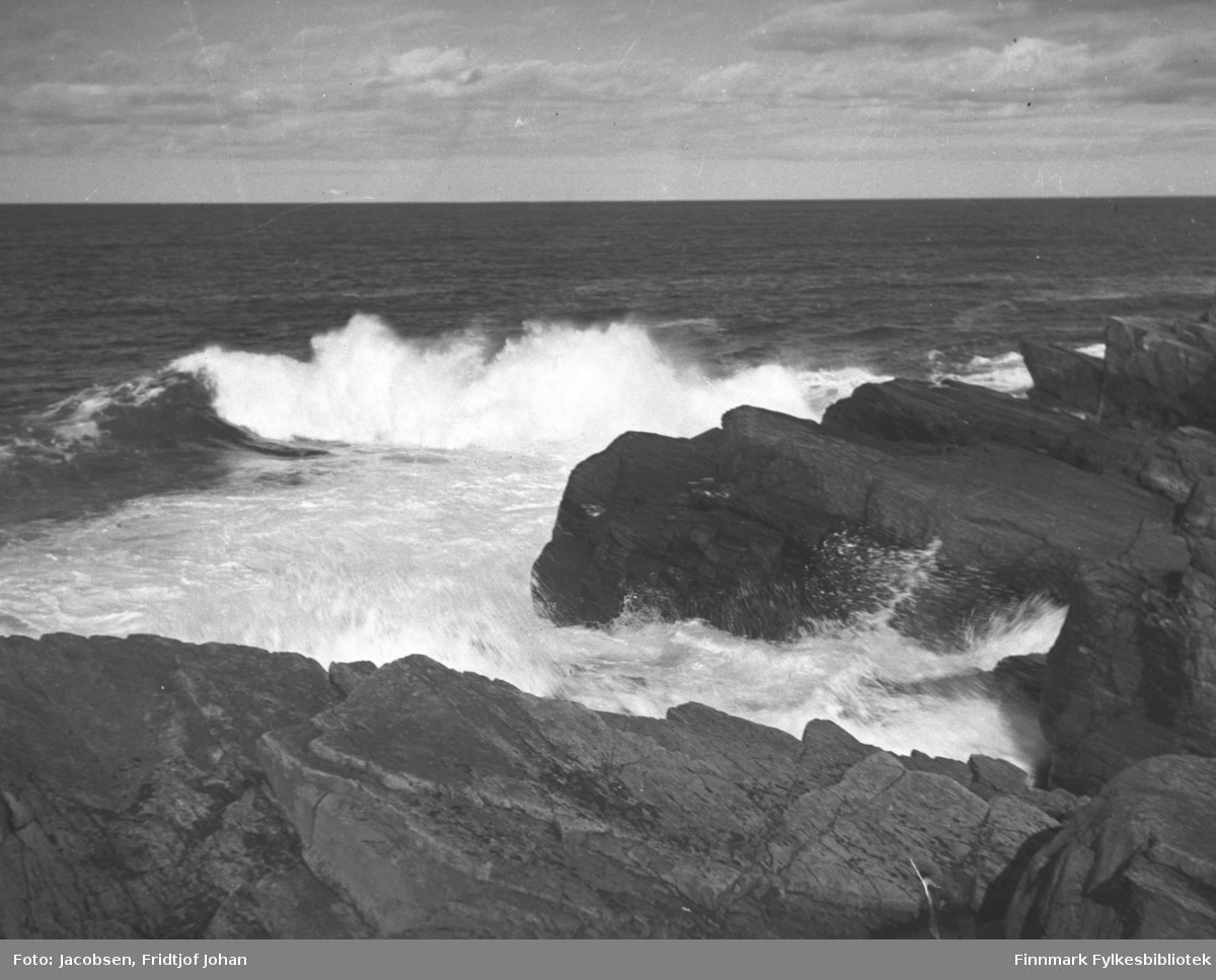 Naturmotiv fra sjøkanten. Bølger slår innover mot et svaberg. Noe skum ligger i sjøkanten.