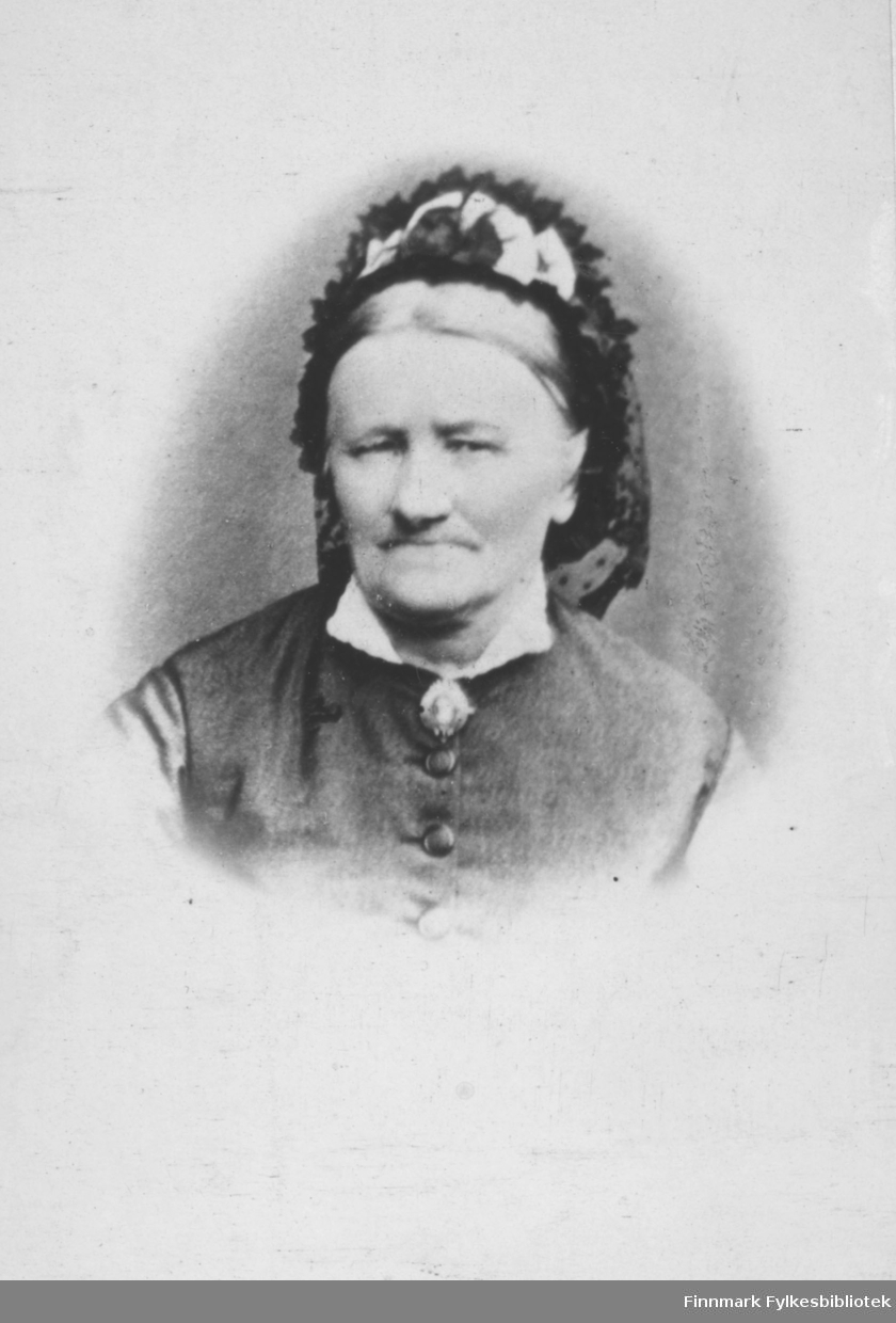 Portrett av Henrikke Vibe. Døde 1892 i Vardø. Hun var mor til Anna Christine Vibe Jacobsen, som var gift med smedmester i Vardø Ole Sigfrid Jacobsen. På bildet er hun kledt i hvit skjorte og vest. Hun har en brosje som pynt i halsen. På hodet har hun et pyntetørkle