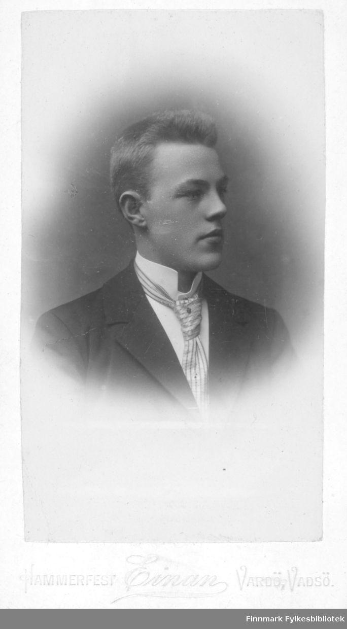 Portrett av en ukjent ung mann. Han er kledt i en mørk jakke og hvit skjorte. Han har et lyst, stripet slips i halsen