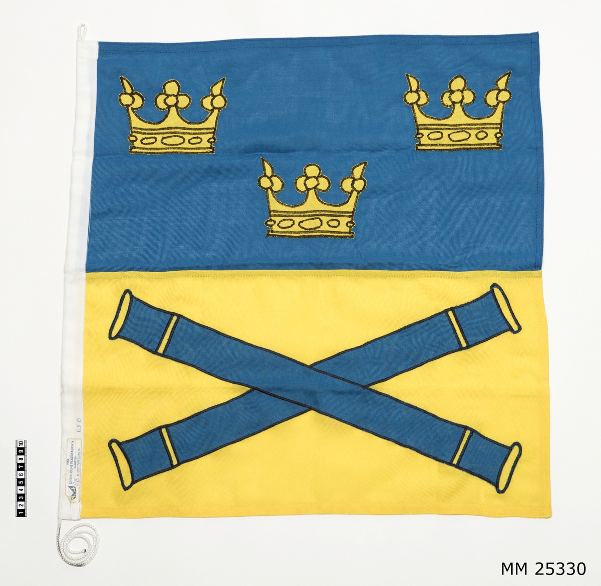 Befälstecken 1,5 dukars, Överbefälhavarens flagga. Flagga av bomull med vitt nylonlik samt vit nylonlina. Rektangulär flagga med två fält. Övre fältet blått med motiv av tre kronor i gult. Nedre fältet gult med två korslagda kanonrör i blått. Liket märkt med lapp: "Nya Stockholms flaggfabrik A/B Tel 232725, 35 Grev Turegatan 35". Samt märkt med penna "ÖB" samt "1,5 D".
