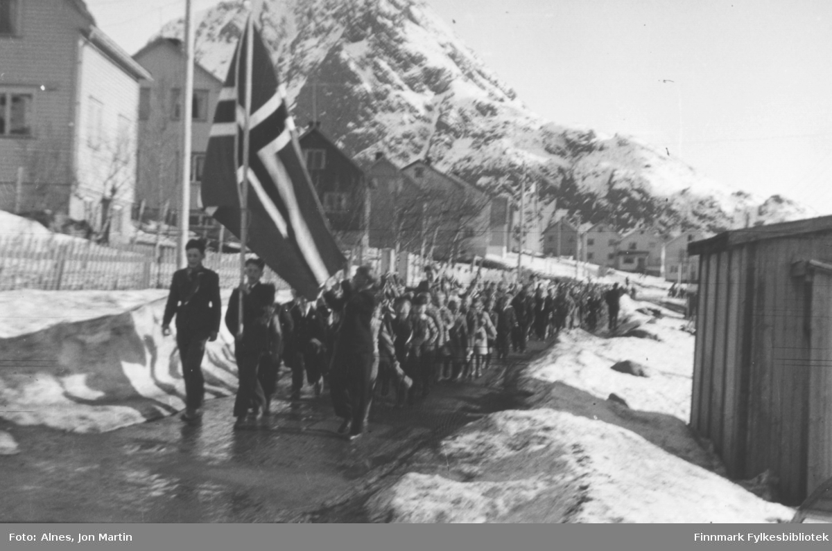 Folketoget 17. mai i Øksfjord, 1954. Da gikk folketoget fra sentrum til kirkegården og retur. Til venstre foran Harald Jensen. Til høyre i bildet: Grønnbrakka der Einar Flåten hadde snekkerverksted