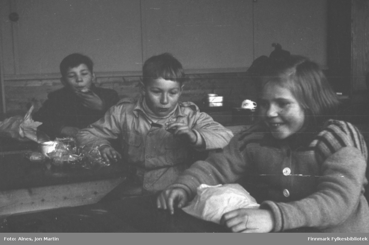 Langfriminutt med spisepause ved Øksfjord Barneskole, våren 1954. Elever med nistepakke i klasserommet, fra venstre: Jens Børve, Gunnar Rydheim og Solfrid Wilhelmsen