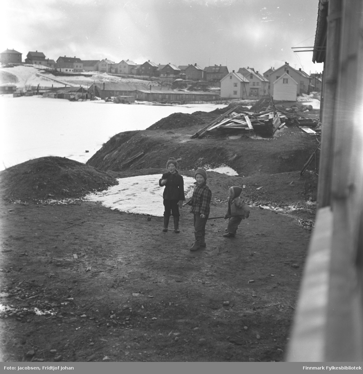 Tre barn leker på det som skal bli Storvannsveien i Hammerfest. Barna er ukjente. Ved bredden av det islagte Storvannet ses brakkene og stallen på området som ble kalt Belsen. Ovenfor de står husene i Moreneveien.