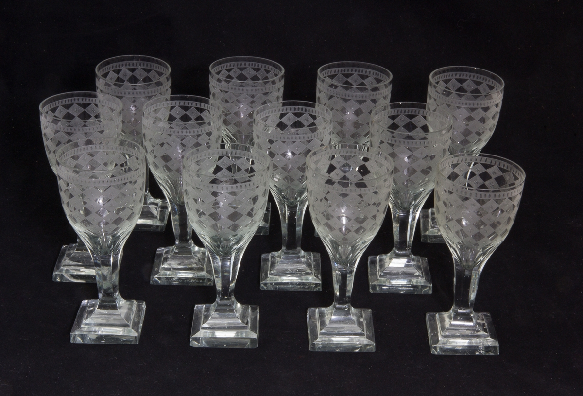 En serie vinglas, 12 stycken, av glas, vars kuppor dekorerade med etsat harlequinmönster och stjärnor. Slipade ben, kvadratiskt slipade fötter.