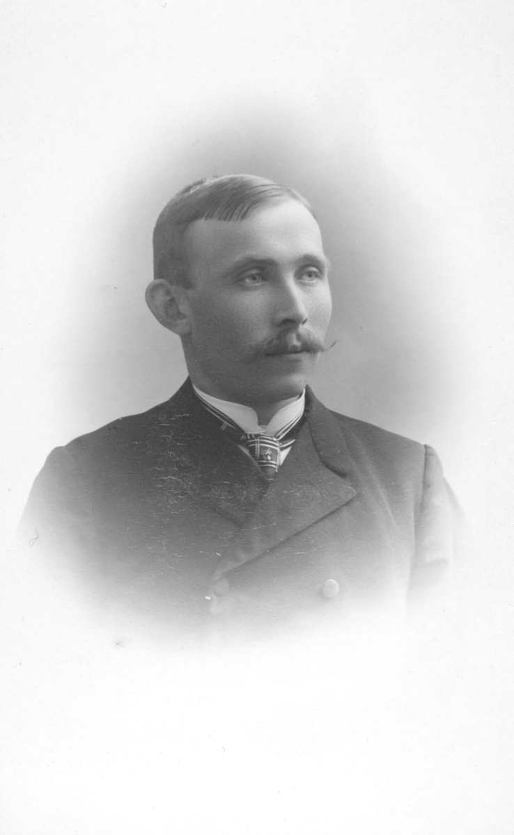 Portrett fra en ukjent mann med stor snurrebart (vokset) og kledd i dobbeltspent dress, skjorte og slips.