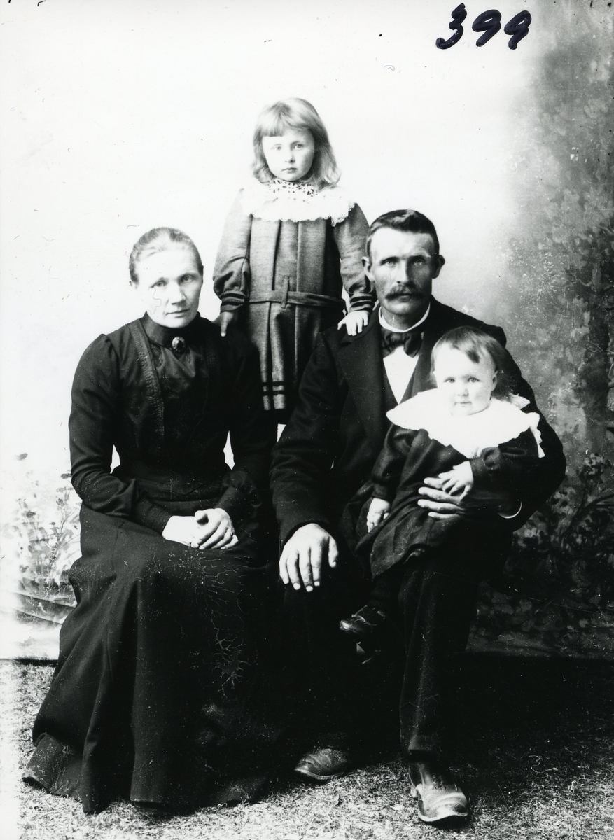 Portrett av kvinne og mann og to barn. Kvinnen er kledd i svart kjole, manne har mørk dress med sløyfe i halsen. Begge barna har hvite heklete krager.