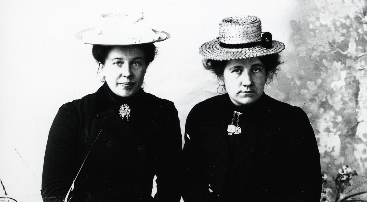 Portrett av 2 kvinner. Begge iført mørke kjoler, sølje i halsen og stråhatt på hodet.