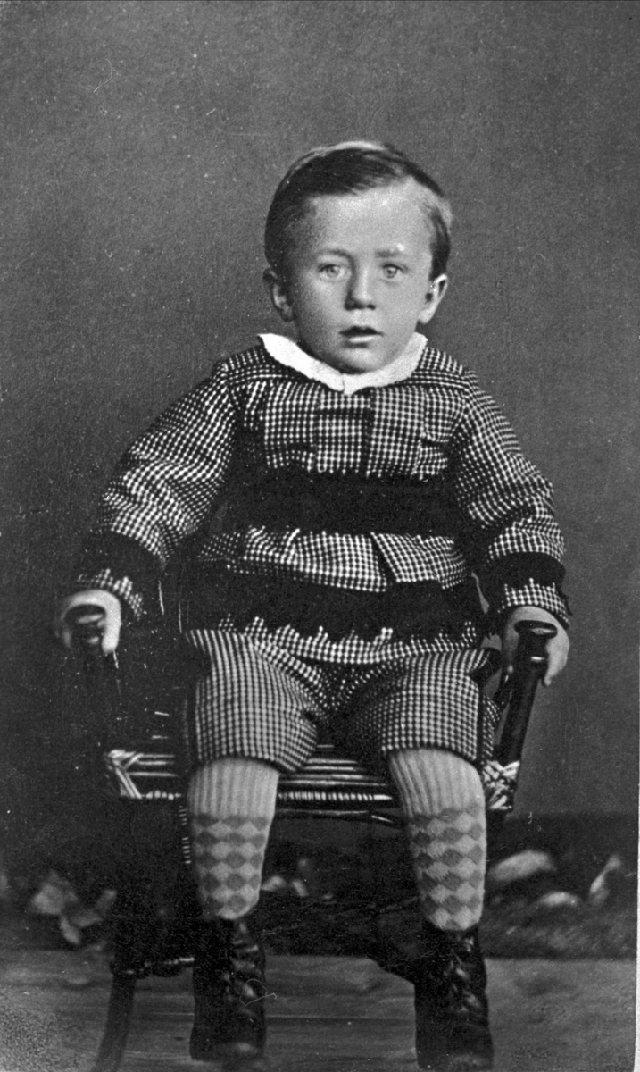 Studioportrett av liten gutt på en stol.