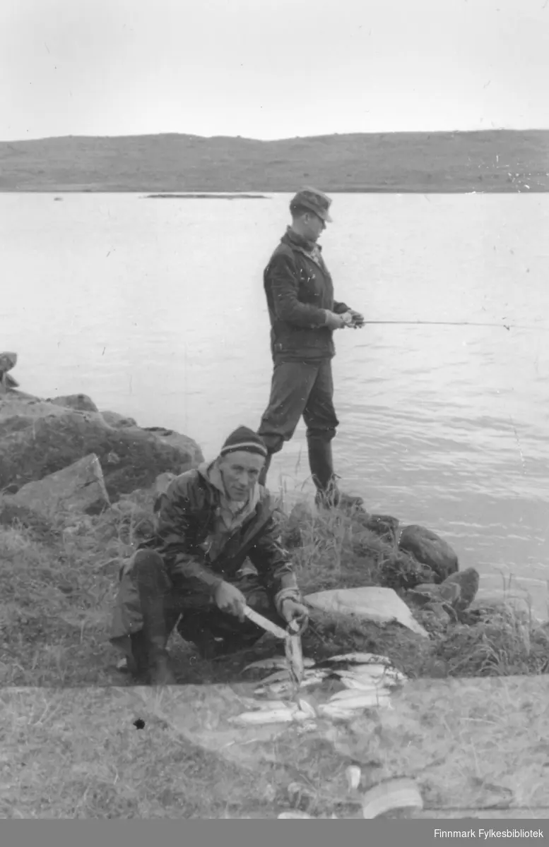 Fotografi fra Vadsø-traktene. Det totalt øde Peskvannet var et ønskested for fiskere. Fisken beit villig og turkompisene sløyde fisken etter hvert som den ble fanget. På dette bildet er Ernst Lebesby i gang med sløying, mens Edvard Irgens fortsatt fisker.