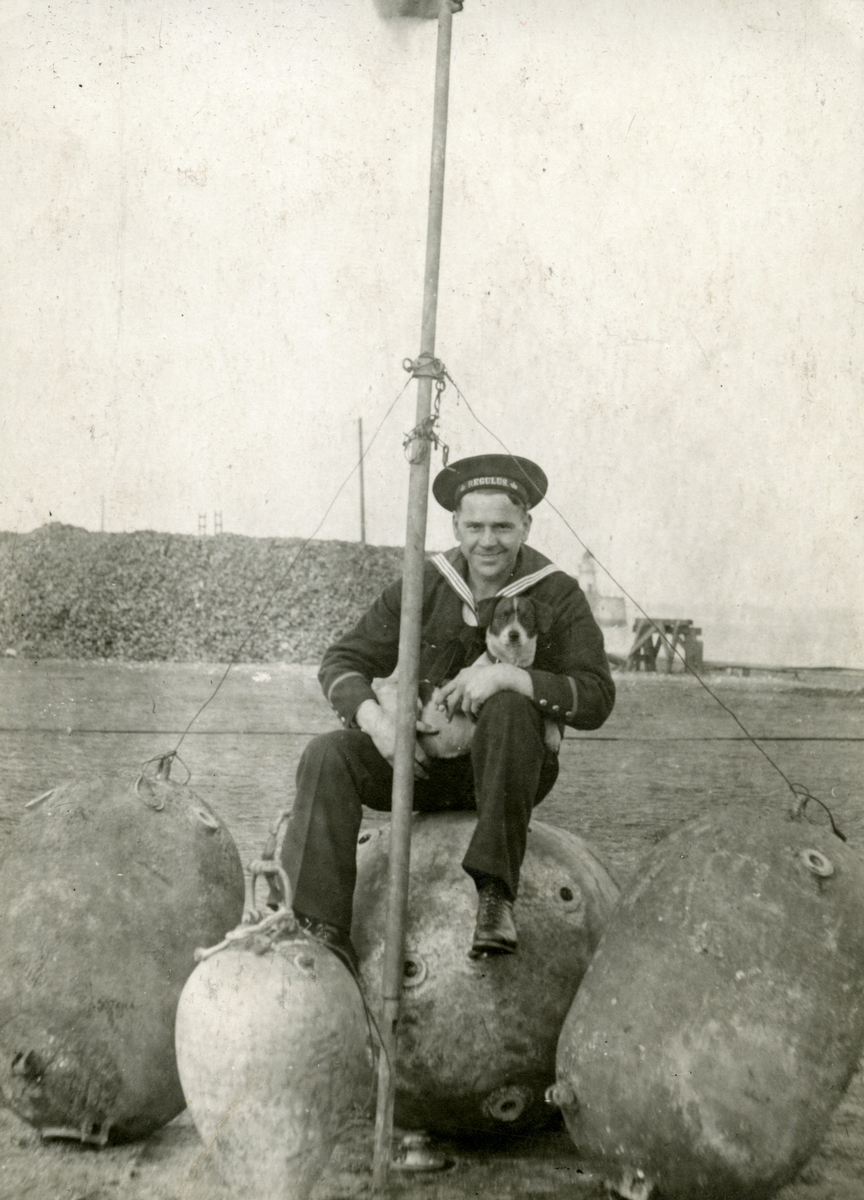 Sjöman med skeppshund i famnen. På sjömannens mössband står texten "Regulus".