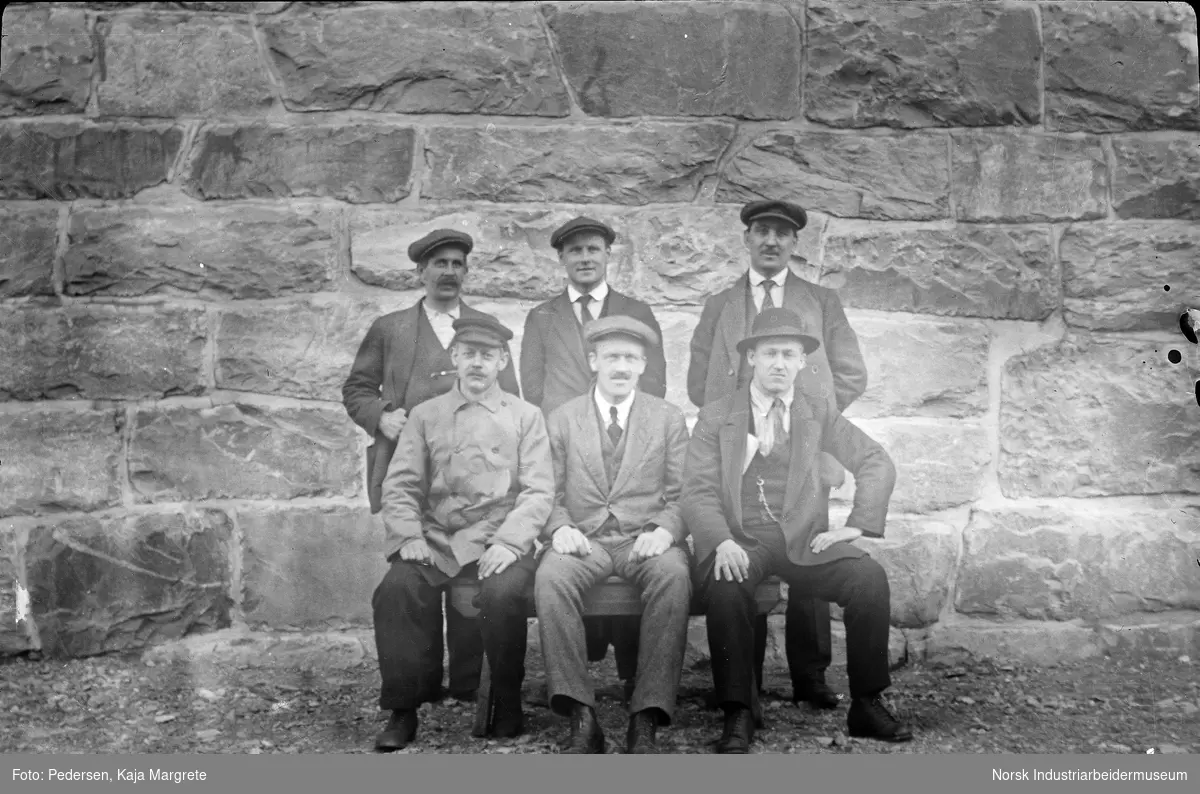 Seks menn oppstillt foran mur på Såheim Kraftststasjon.  Mennene er kledd i dress og hatt, antagelig ingeniører og funksjonærer.
