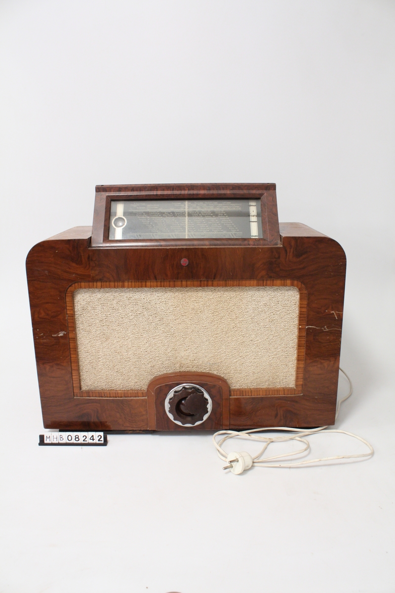 Philips radioapparat fra omkring 1939. Trolig kjøpt hos Brommeland. Innlevert til tyskerne under krigen. Plate på toppen dekker søkerskala som kan vippest opp. Nederst midt i front en skruknott for innstilling av frekvens.