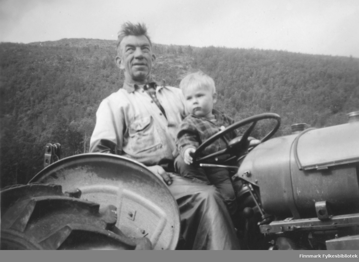 Kristian Wisløff pløyer jorda for en familie i Alta. Her ser vi han sittende på en David Brown-traktor med en liten gutt på fanget. I bakgrunnen ser vi en skogskledd høyde i terrenget