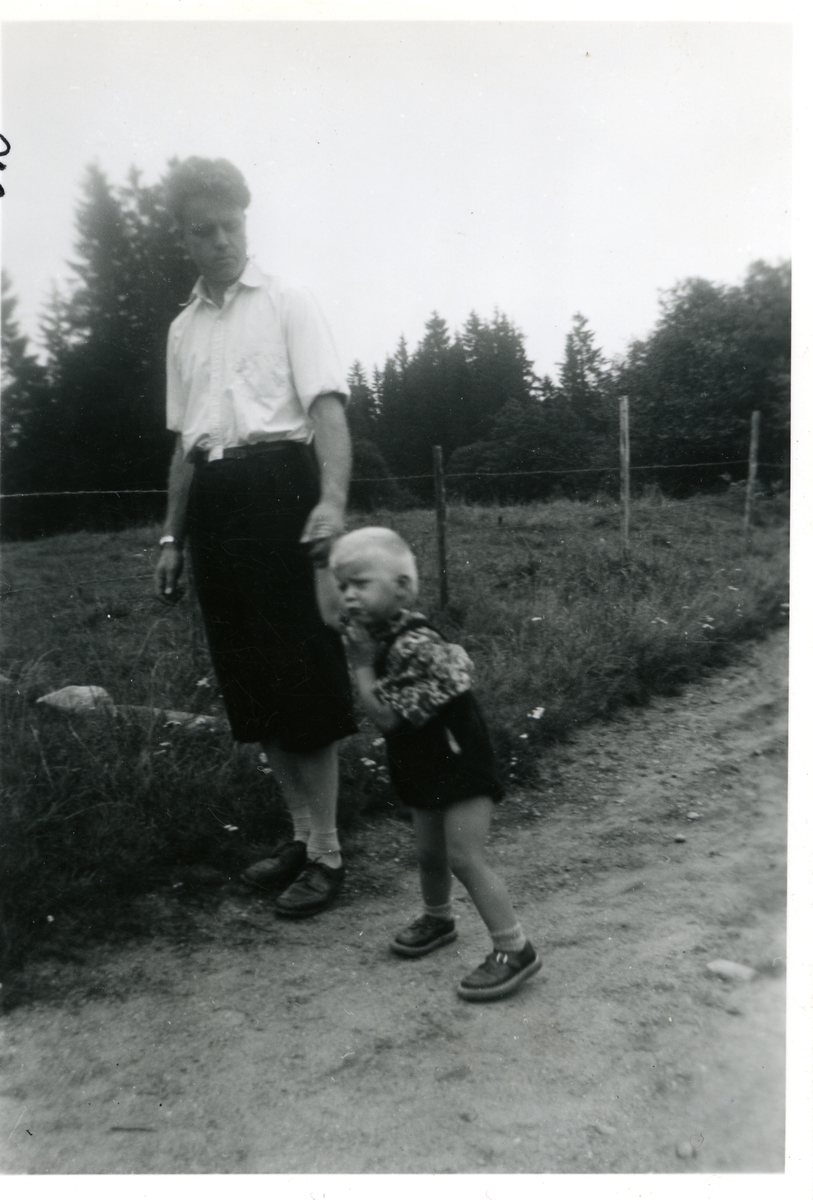 Mann og barn stående på en grusvei, ved siden av et gjerde