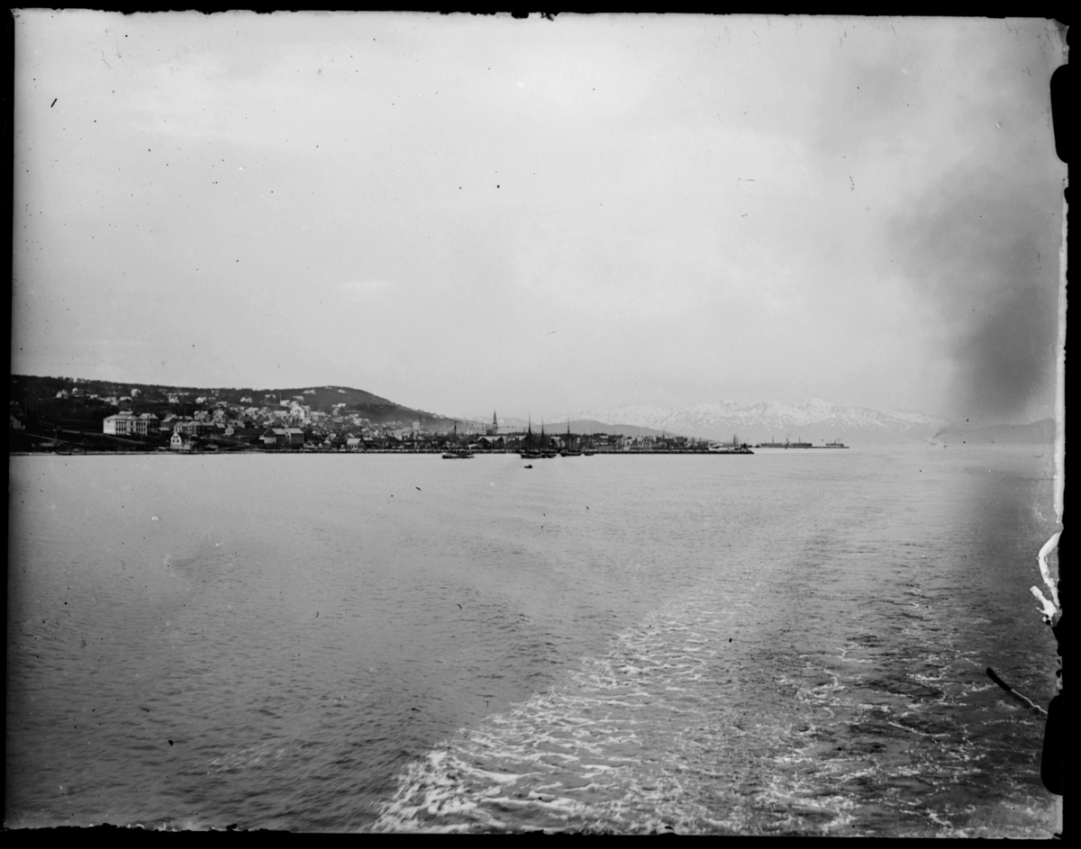 Bildet er tatt fra sjøen. Vi ser en by, anntagelig Tromsø. Et dampskip i det fjerne. Muligens fra reisen nordover i 1912