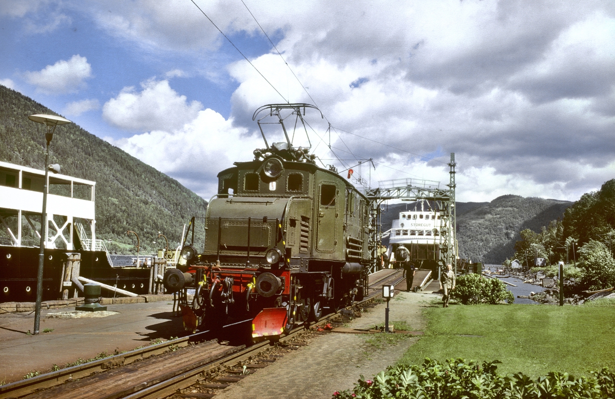 Rjukanbanen, Norsk Hydro. Elektrisk lokomotiv RjB 14 (NSB El 1 2001) på fergeleiet ved Mæl. Jernbanefergen M/F Storegut har lagt til kai og vognene skal skiftes av fergen med skiftetau. Til venstre D/F Ammonia.