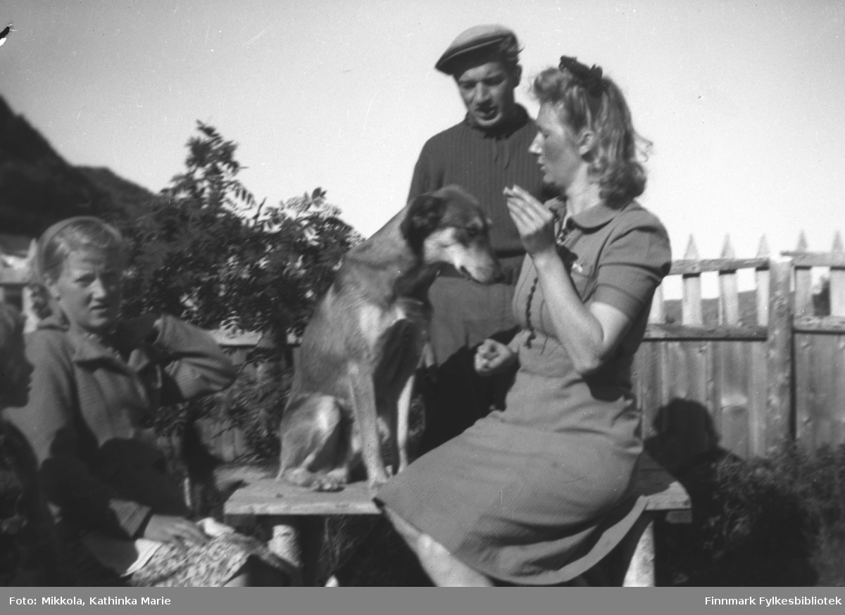 I hagen på Mikkelsnes, ca. 1942. Marine Mikkola med en tiggende hund til høyre. Herlaug Mikkola til venstre, og bak står Andreas Mikkola