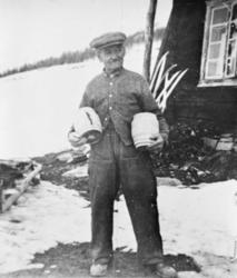 Eldre mann står utendørs, Syver bærer et hjulnav i hver arm,