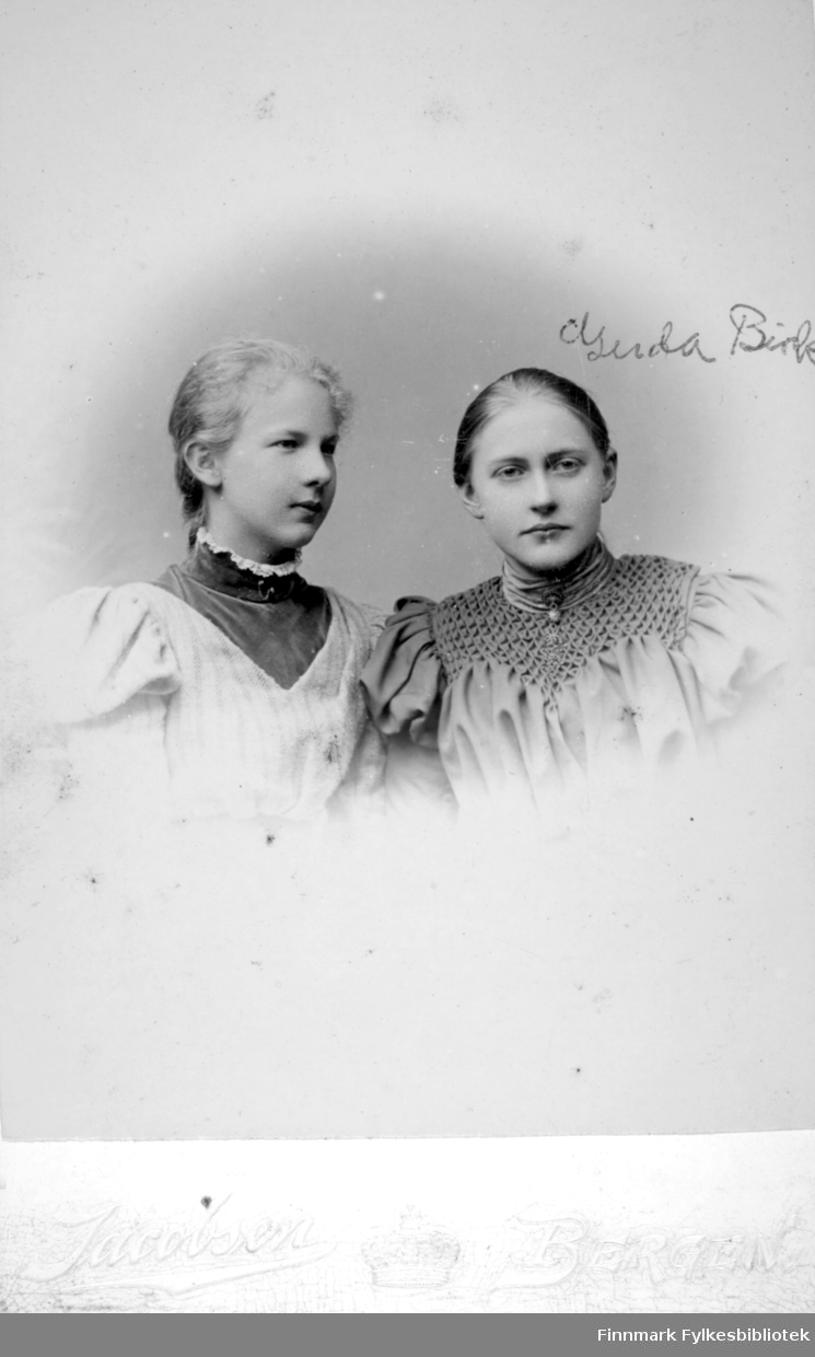 Portrett av to unge damer, Gerda Buck til høyre på bildet. Damen til venstre har en lys overdel med et mørkere parti i halsen og en smal blondekrage. Gerda har en mørkere overdel med tøymønster og høy krage.