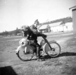 En ung mann sitter på en moped/lett motorsykkel en solfylt s