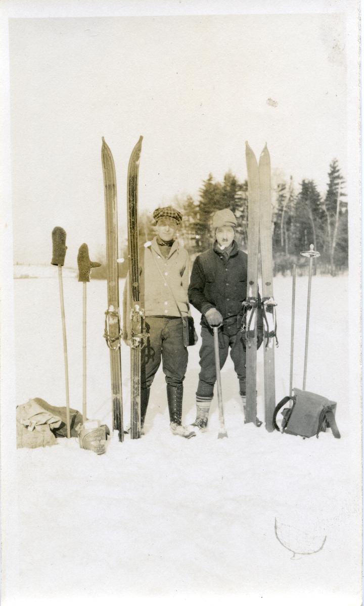 To menn oppstilt på isen. De har ski, staver og sekk ved siden av seg.