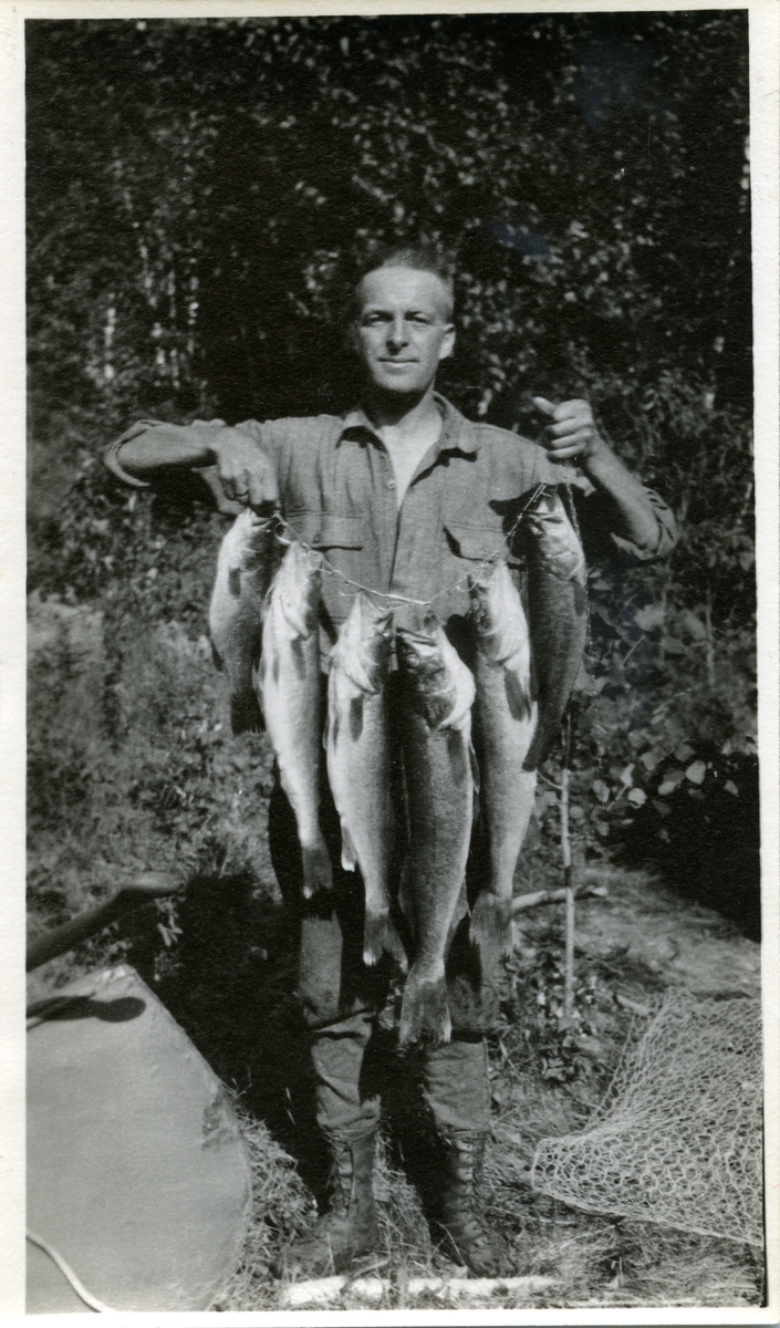 Foto av mann som holder 6 store fisker foran seg. Fangsten er tredd på en snor el.l.