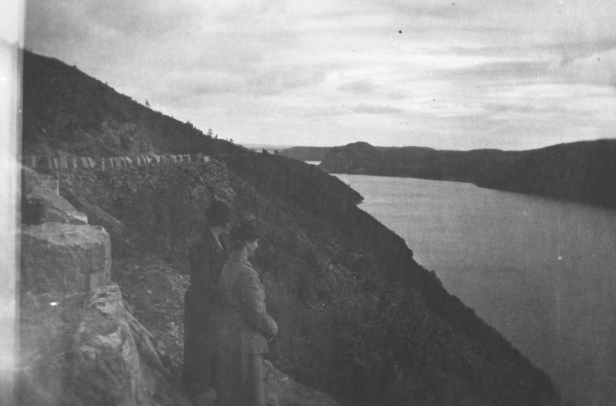 To kvinner som står og ser utover en elv, muligens er det Pasvikelva