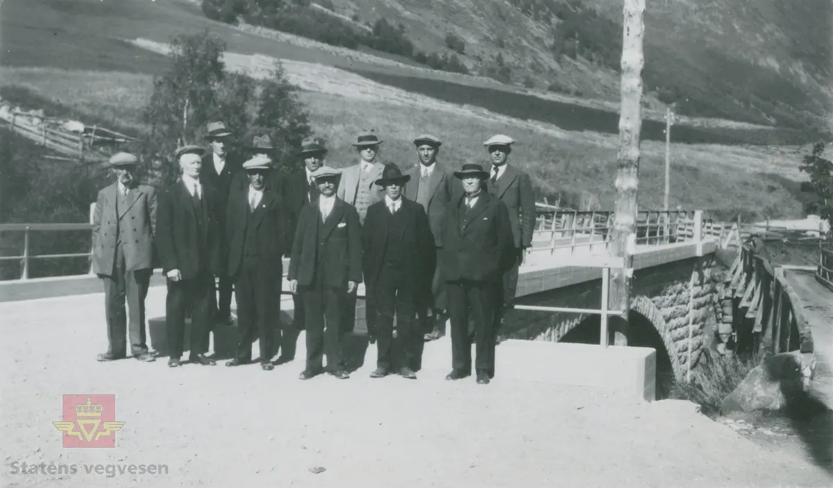 Album fra 1929-1943. En gruppe dresskledde,  staute menn med hatter og sixpenceluer på hodet. Sannsynligvis en  befaring på ferdigstilt bru. Hoftabru i Lom 1934.