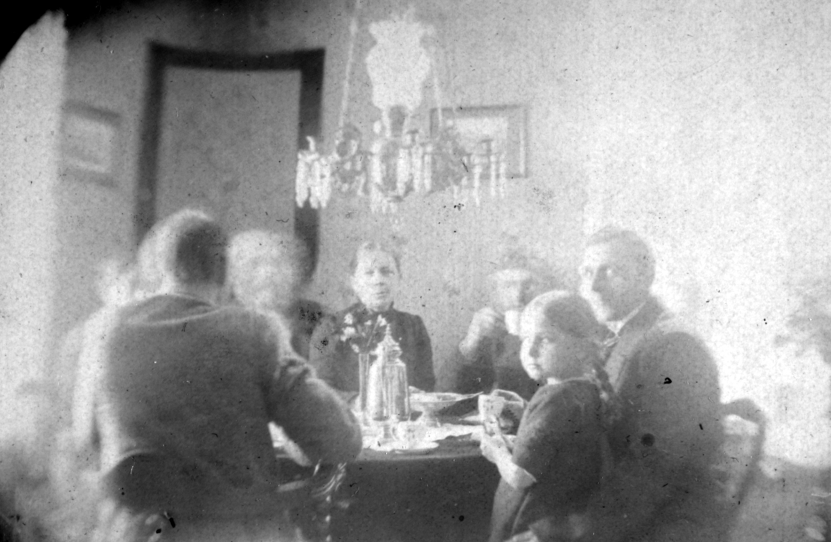 Håheim-familien i Neiden sitter rundt et bord. De fleste personene på bildet er ukjent, men mannen til høyre kan være Reidar Håheim. Han er kledd i jakke og slips. I hans fang sitter en en liten jente i kjole. Over bordet henger en lysekrone.