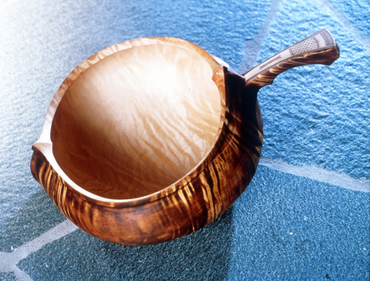 En rikule av bjørk. Arbeidet er en tradisjonell samisk reinmelksbolle. Skaftet har horninnlegg med skåret dekor.
