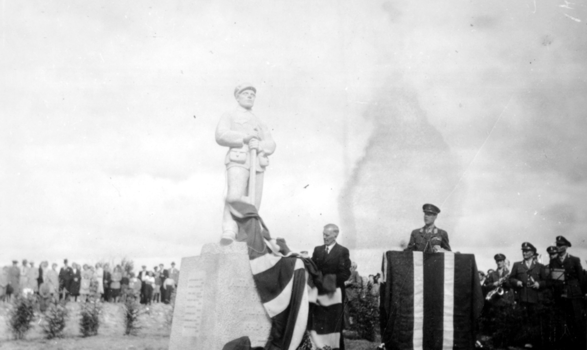 Generalmajor A. D. Dahl taler under avdukingseremoni av bauta til minne for de falne i Alta bataljon under krigen. Statuen ble avduket 24.7.1949.  Til høyre kan man se divisjonsmusikken.