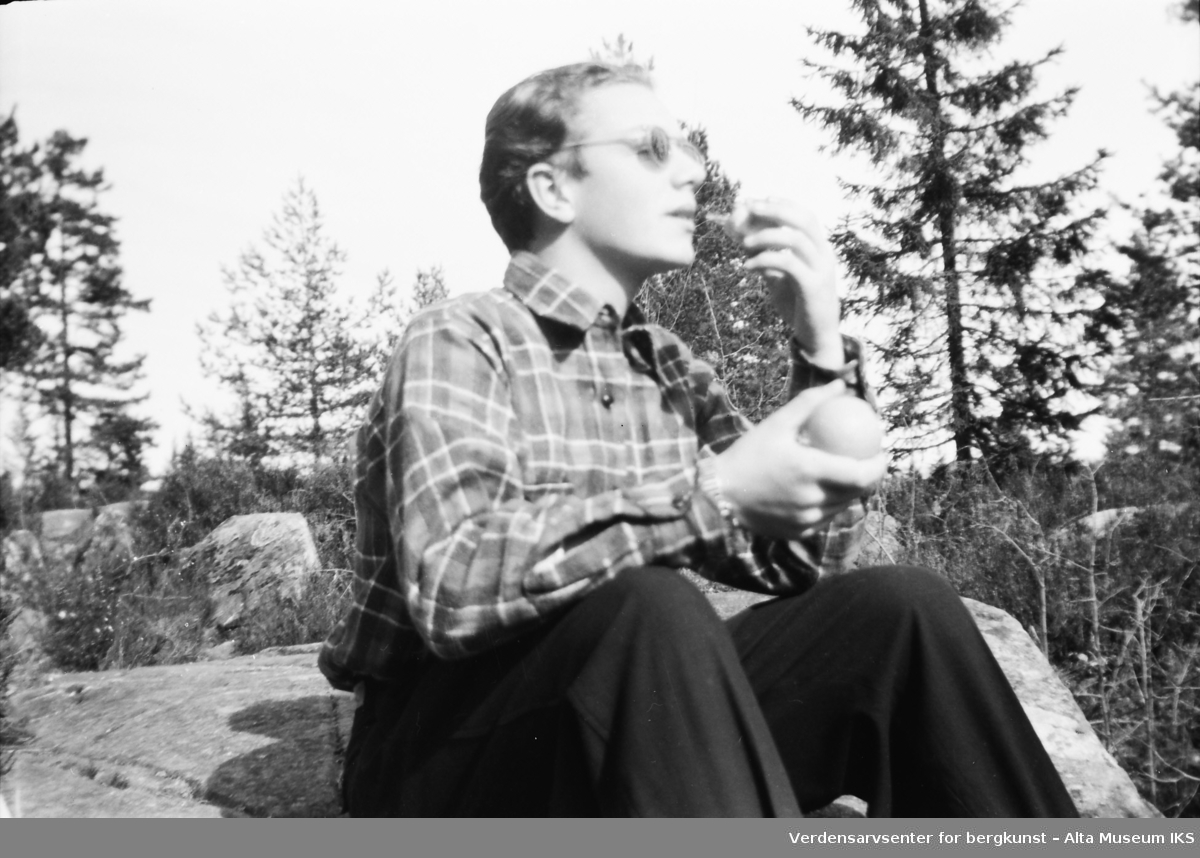 En ung mann med solbriller sitter på en sten og spiser.