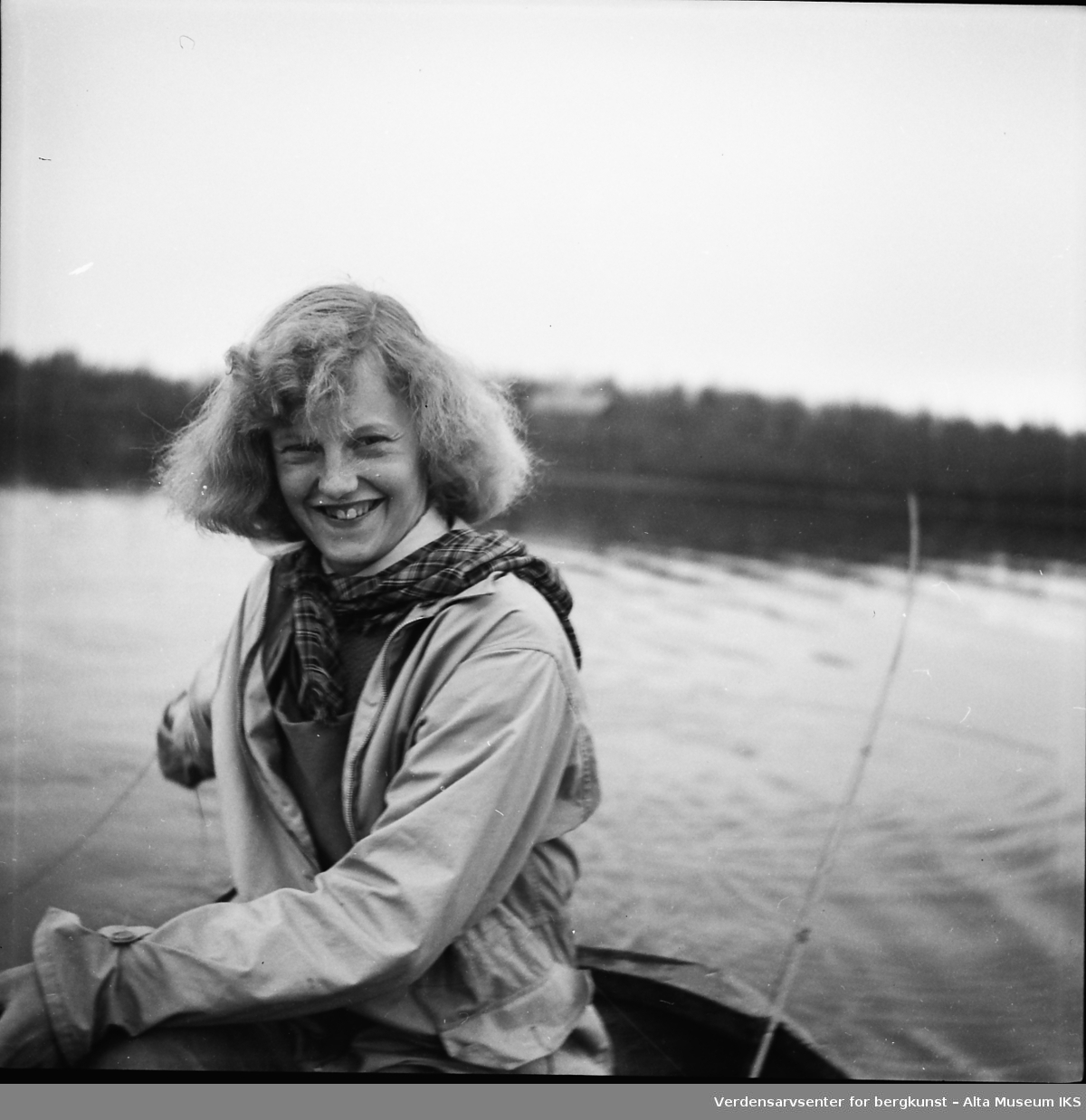 En ung kvinne sitter i en båt midt på et vann, og smiler lurt til kameraet.