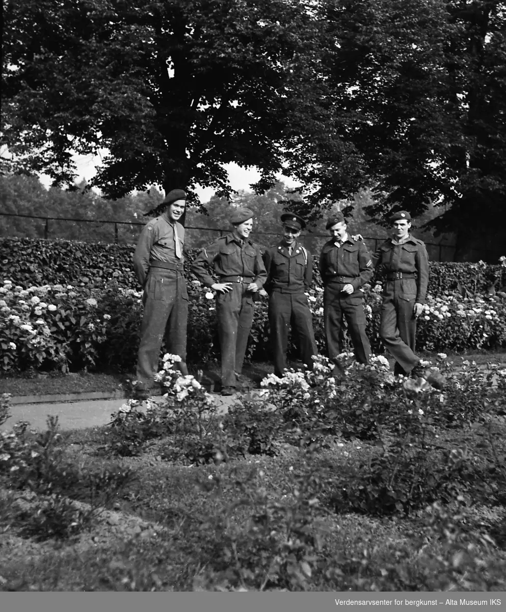 Fem soldater står på en gangvei. Bak og foran soldatene blomstrer floraen.