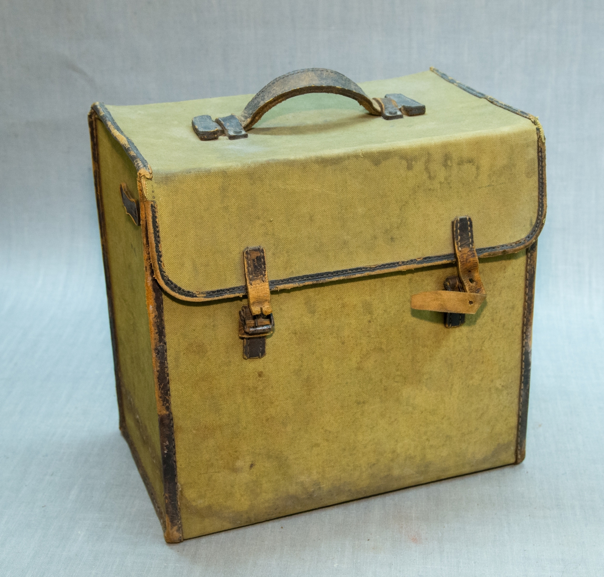 Firkanta koffert i olivengrøn kraftig bomull, kantar og hank i skinn. Inneheld uregistrerte blitzlampar og diverse utstyr for lampar
