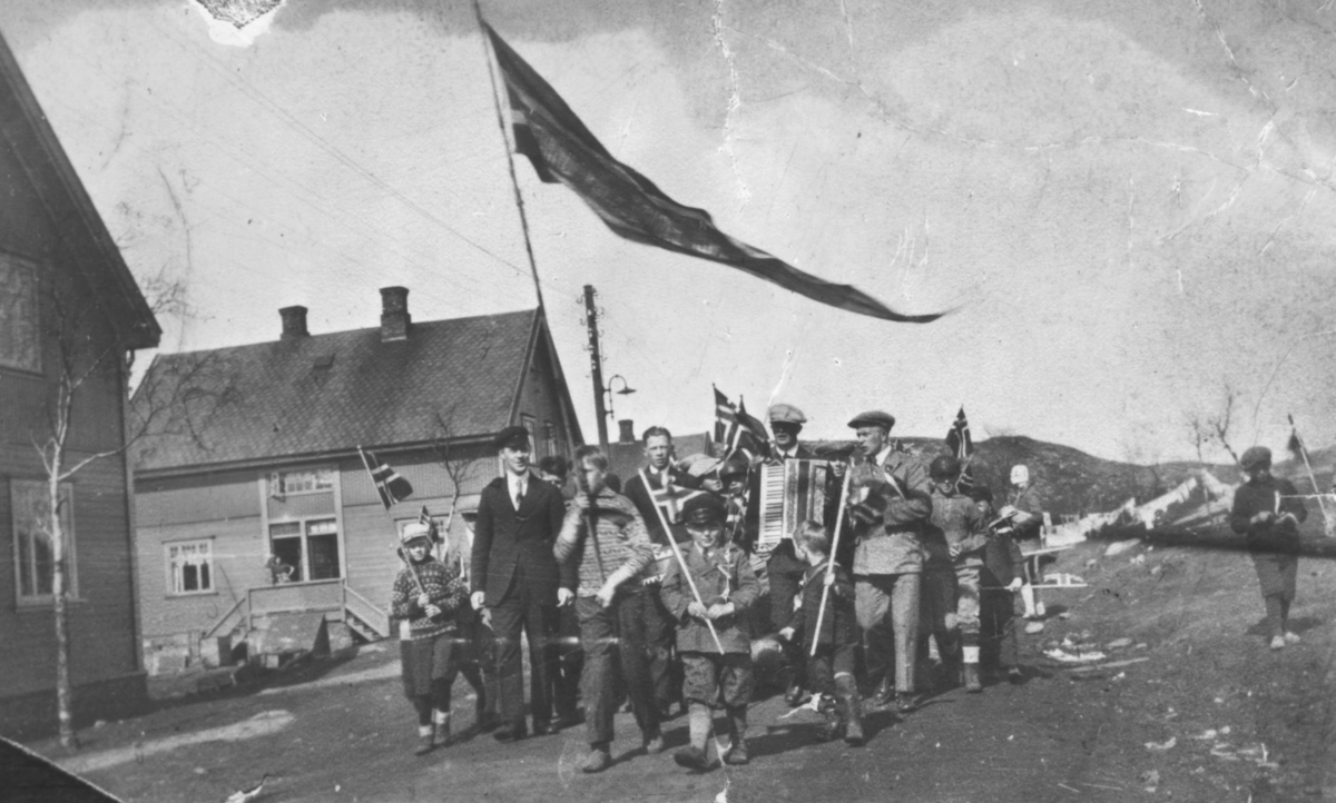 17.mai i Bjørnevatn, 1929. Flere av personene er navngitte. Et lite tog med fane først. Skolestyreren er med, og trekkspillmusikk. Klærne er ganske enkle.