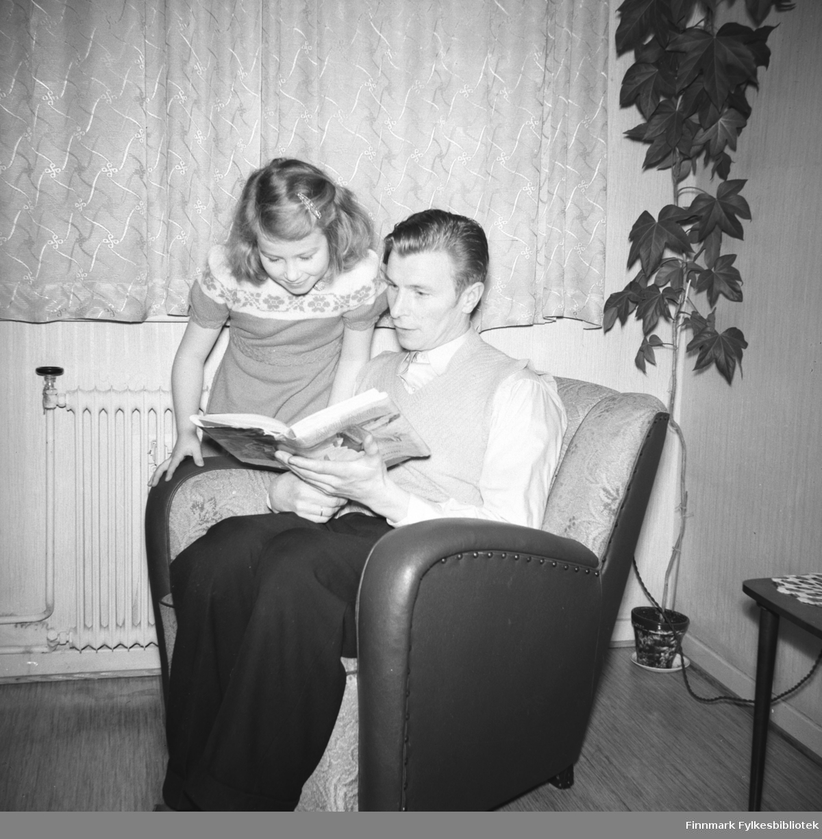 Eino Drannem med sin datter Turid Lillian sitter i lenestolen og leser ei bok