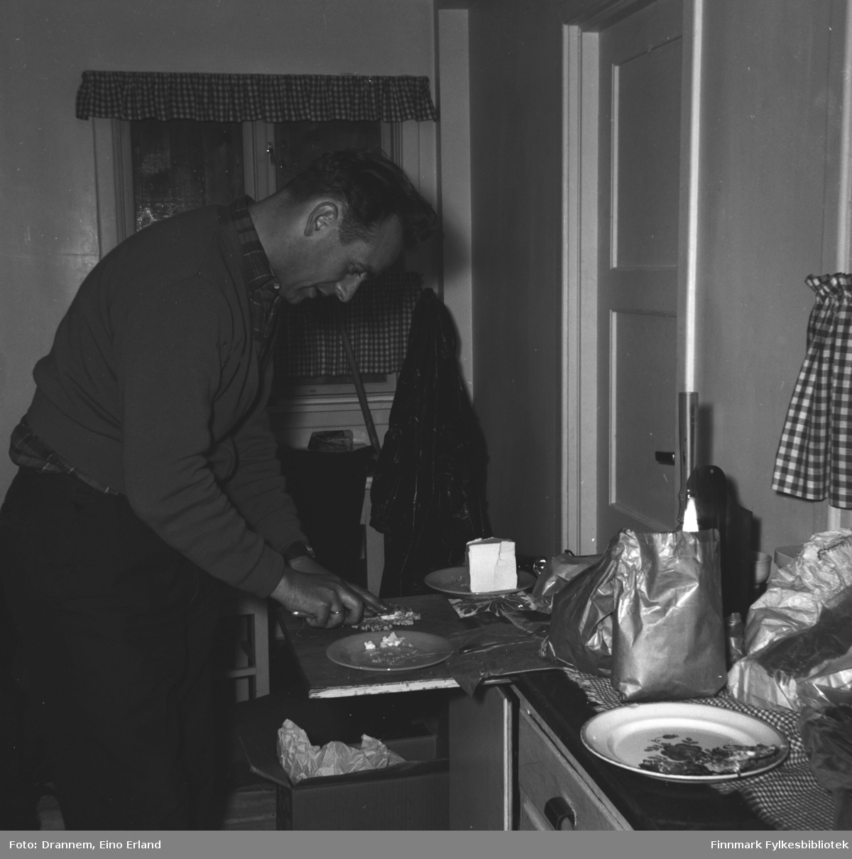 En mann (Jakobsen?)smører brødskviver i kjøkkenet. Bildet er tatt sannsynligvis i Hammerfest