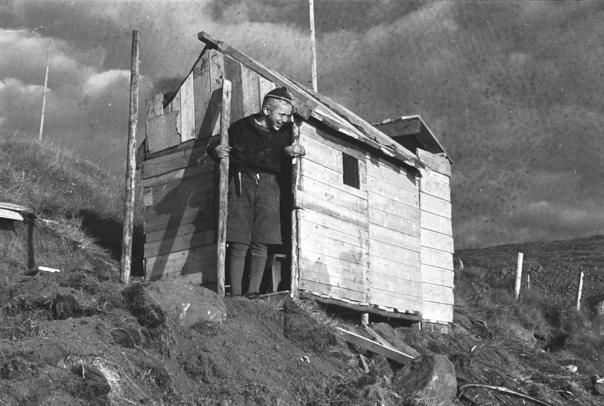 En gutt står ved siden av en lekehytte som sannsynligvis er bygget av materialrester fra gjenreisningsbygg i Honningsvåg etter andre verdenskrig.

Arkitekt Ola Hanche-Olsen arbeidet ved Brente Steders Reguleringskontor i 1946. Hovedadministrasjon for gjenreisning av Nord-Troms og Finnmark ble lagt til Harstad og fikk navnet Finnmark kontoret. Landsdelen Nord-Troms og Finnmark blev oppdelt i syv distrikt med hver sin administrasjon. Honningsvåg, distrikt IV, skulle betjene Nordkapp, Lebesby, Porsanger og Karasjok kommune.

Ola Hanche-Olsen har tatt bildene. Han var født 13. mars 1920 i Borre, død 11. februar 1998 i Gjettum. Han var både arkitekt og barnebokforfatter. Han hadde artium fra 1939, arkitekteksamen fra NTH 1946 og arbeidet deretter ved Finnmarkskontoret 1946–48 før han etablerte egen arkitektpraksis. Han debuterte som barnebokforfatter i 1974 med lettlest-boka "Knut og sjørøverne", og skrev i alt 12 bøker. Han var XU-agent 1944-45, og var også en aktiv fjellklatrer og friluftsmann. Ola var gift med Solveig Hanche-Olsen (f. Falkenberg); de fikk 3 barn, blant dem matematikeren Harald Hanche-Olsen.

