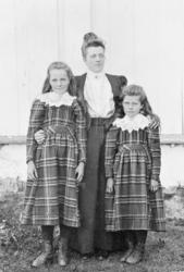 Kvinne og to ungjenter ute ved husveggen, det er sommer.