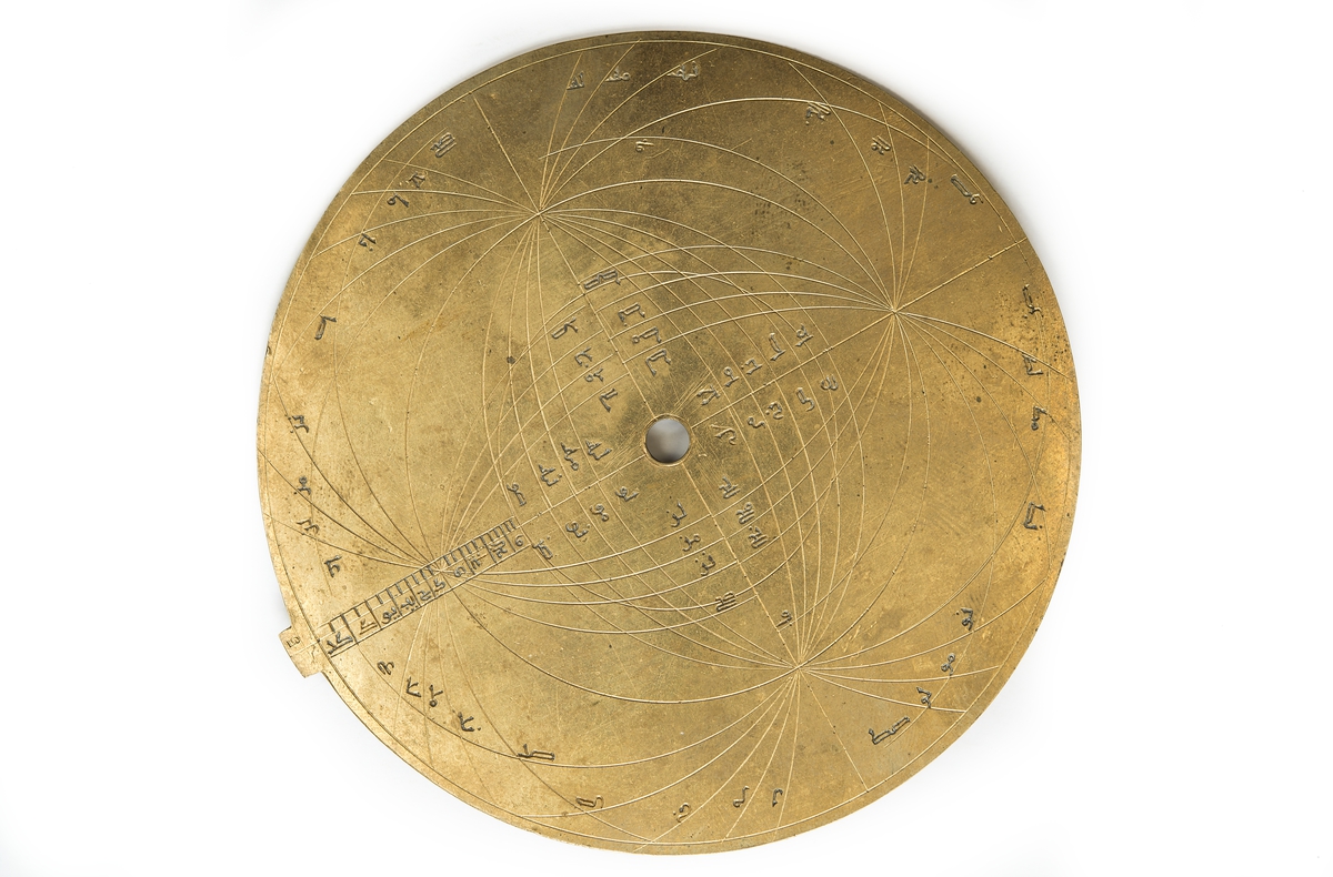 Made of brass n 729 A.H. (after Hedschan) =year 1328-29. 
It was bought it in Marocco in 1907 and was made by Ahmad ibn Ali Sarafi in Spain, Alcalá (nearby Sevilla).
The practical use of the astrolabe is to find the time during the day or night (by altitude of the sun or the stars) and the time of a celestial event such as sunrise or sunset and as a handy reference of celestial positions.
The astrolabe is made up of several separate parts. The main-part is a disc of brass called the Mother (Mater). Into the Mater fits seven thin discs, called the plates or tables. The seven plates are each engraved and represent the usual projection of the sphere varied only for the particular latitudes for which each was made.