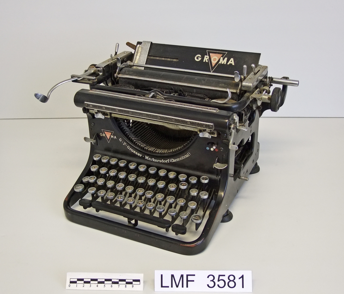 Tysk skrivemaskin med norsk tastatur. Nedleggbar linjal;  øverst bak støtteplata.

Form:  rektangulær